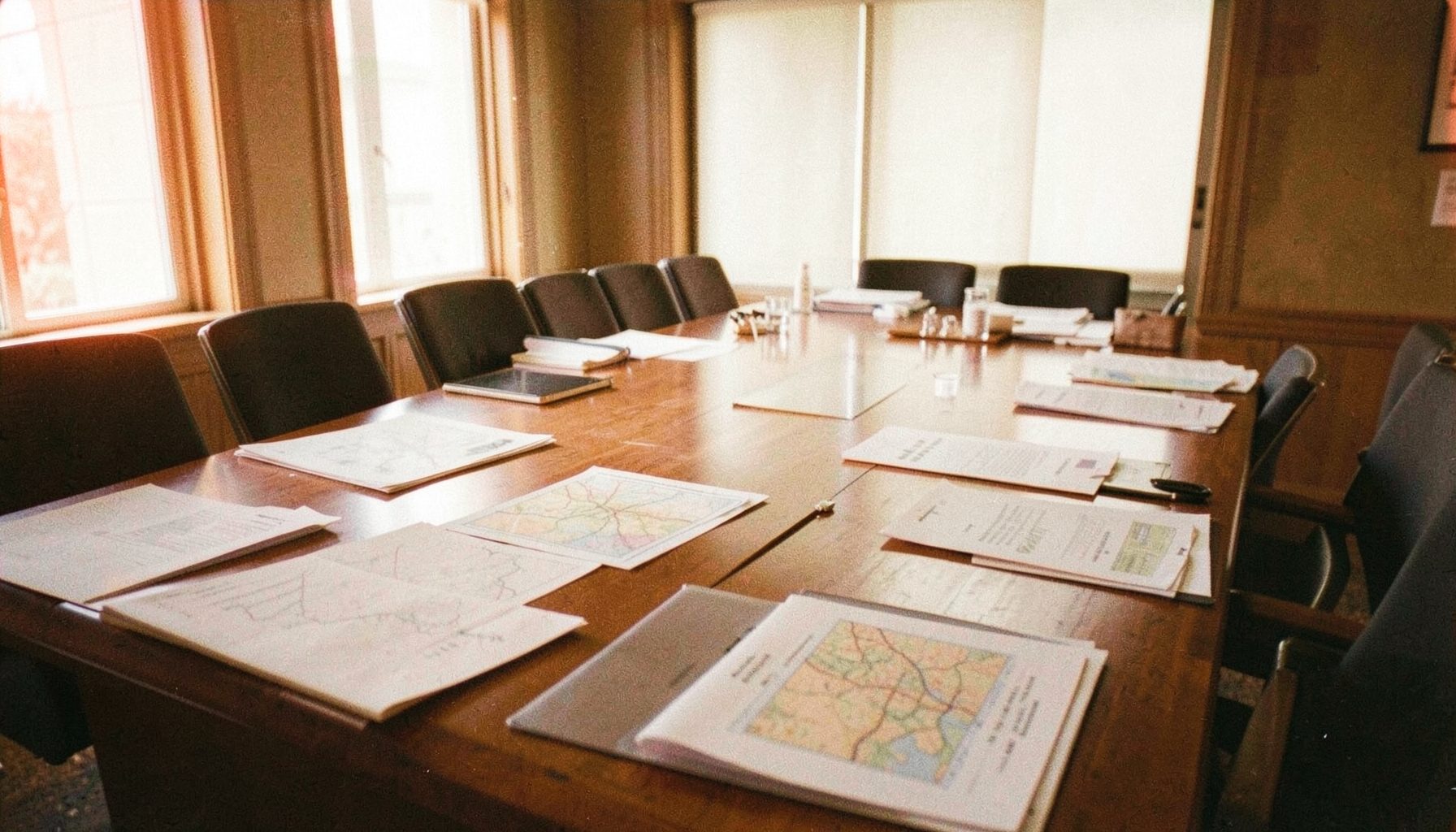 Conference room with maps and policy documents spread across a large table, warm wood tones and soft daylight from windows